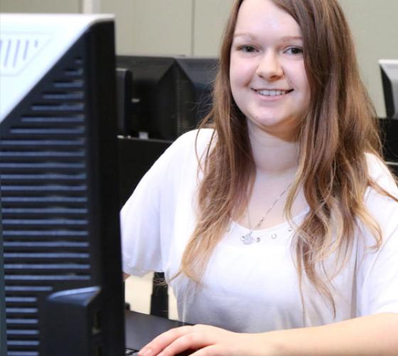 student smiling and siting at workstation computer