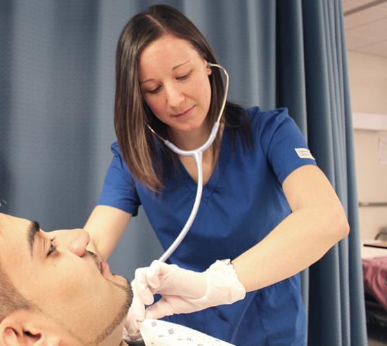 Nursing student with stethoscope in ears checking patient's vital lying down in hospital bed