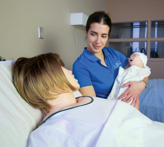 Nursing student holding mannequin baby beside mother mannequin in maternal child simulation lab