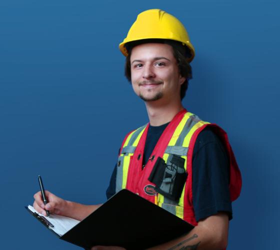 Outdoors student in hard hat and safety vest holding clipboard and pen