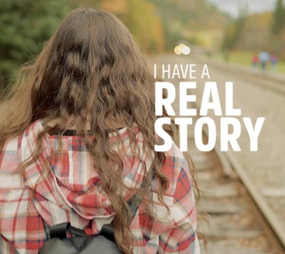 Real Story image of graduate walking away on train tracks with her back facing the camera