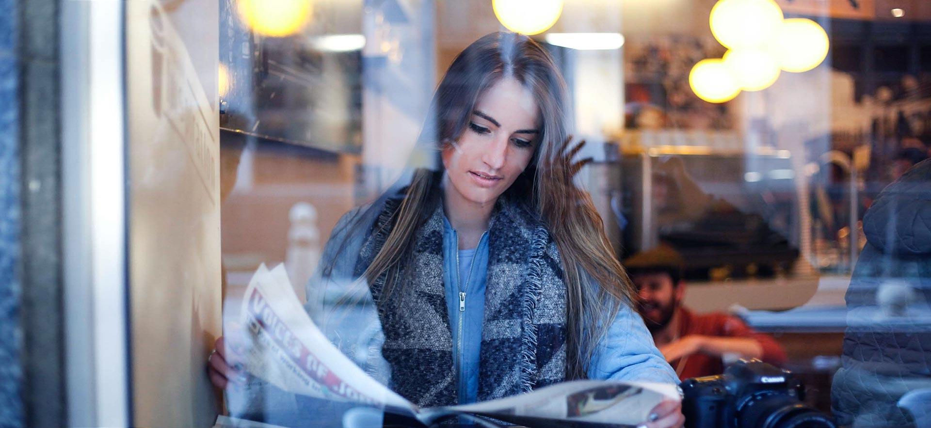 Young woman reding a newspaper in a cafe.