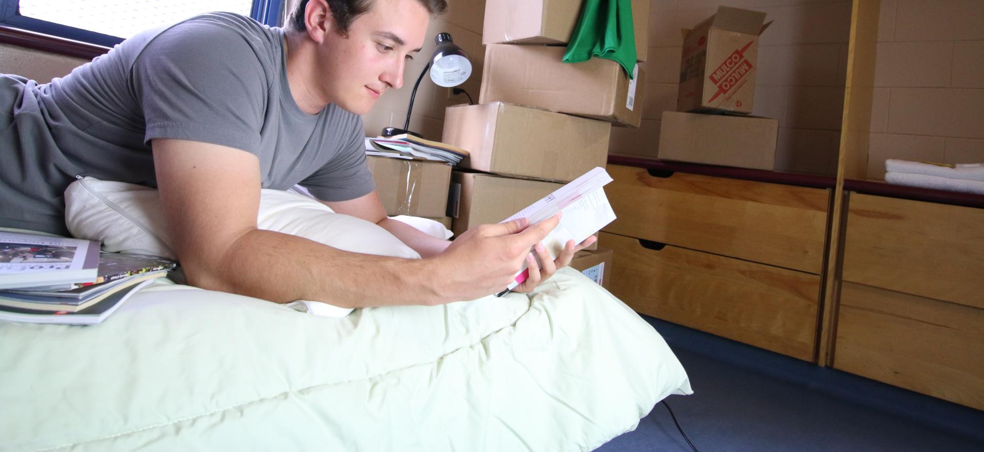 Student laying in bed reading book