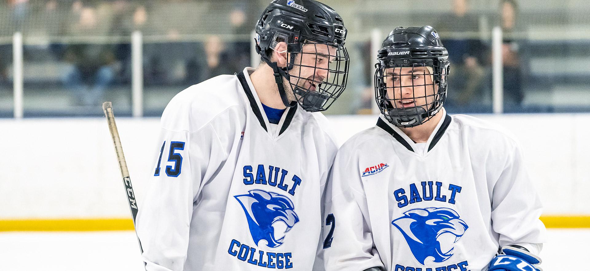 Two male cougar hockey players stop and talk.