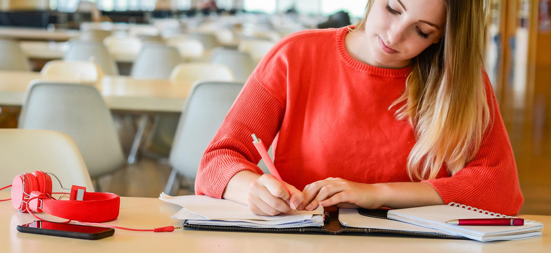 female student writing in notebook sitting at a table