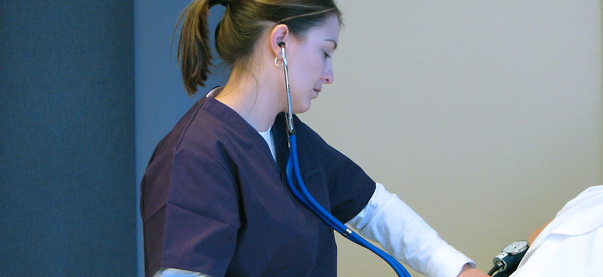 nurse with stethoscope measuring blood pressure on a patient