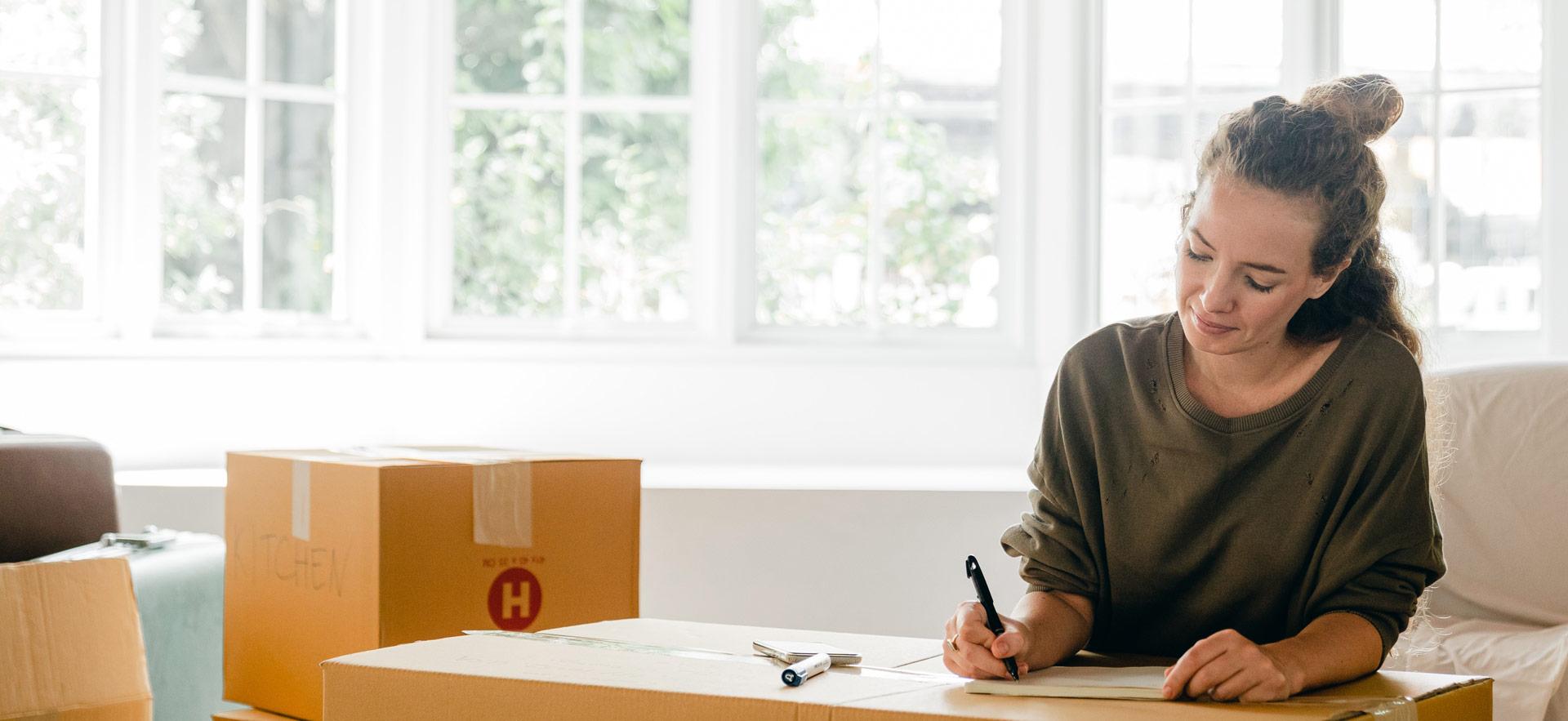 female in a home making notes on a moving box