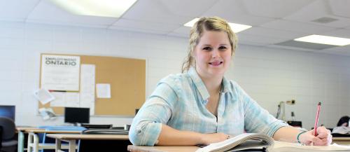 One female Academic Upgrading student smiles while sitting at her desk in class.