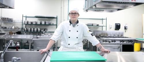 Culinary student in uniform posed at counter in culinary lab looking at camera